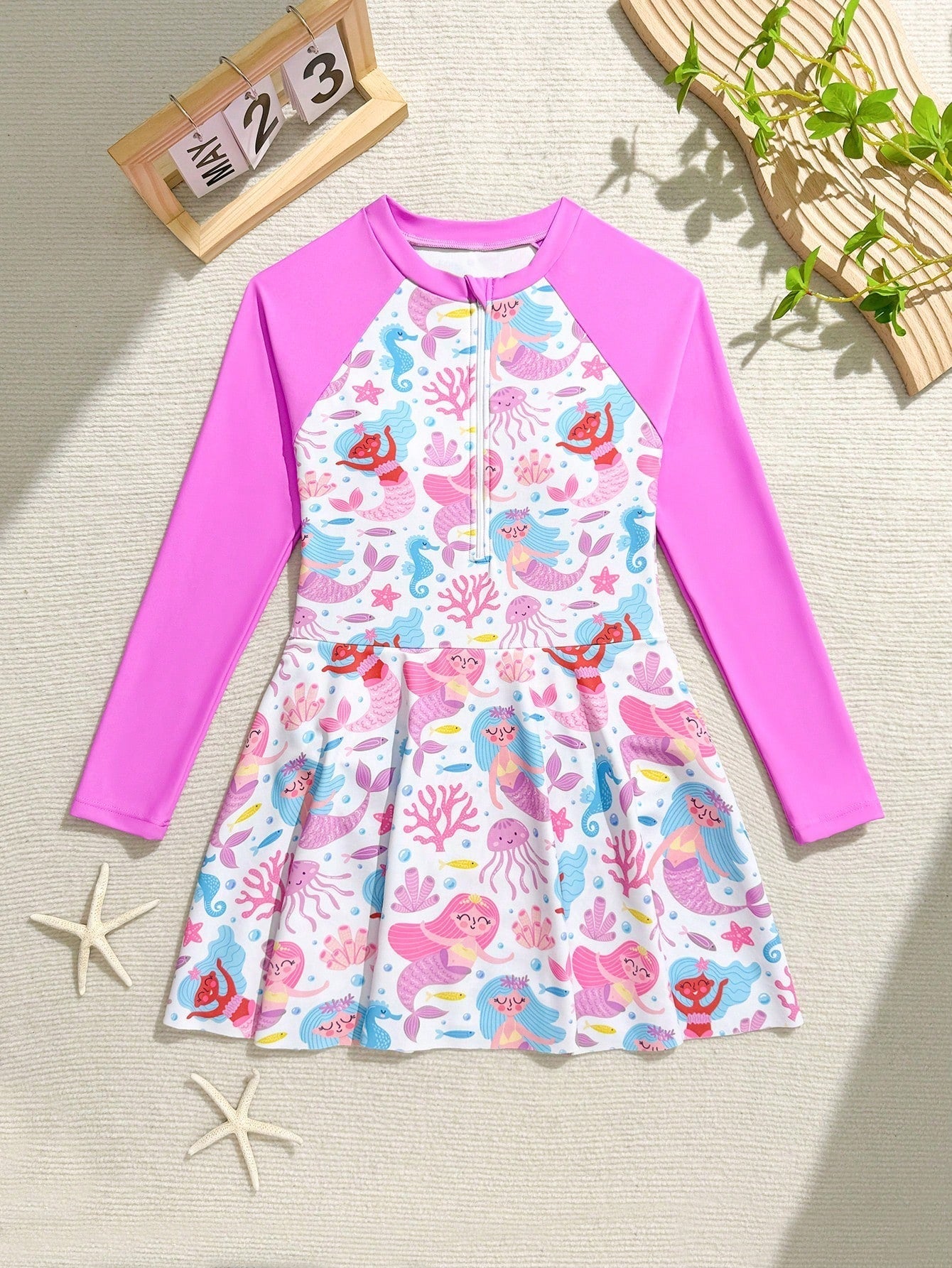 Tween girls one-piece rash guard swimsuit with long sleeves, high neck, front zipper, and ocean shell graphic print in a fitted style for beach, swimming, and vacation wear.