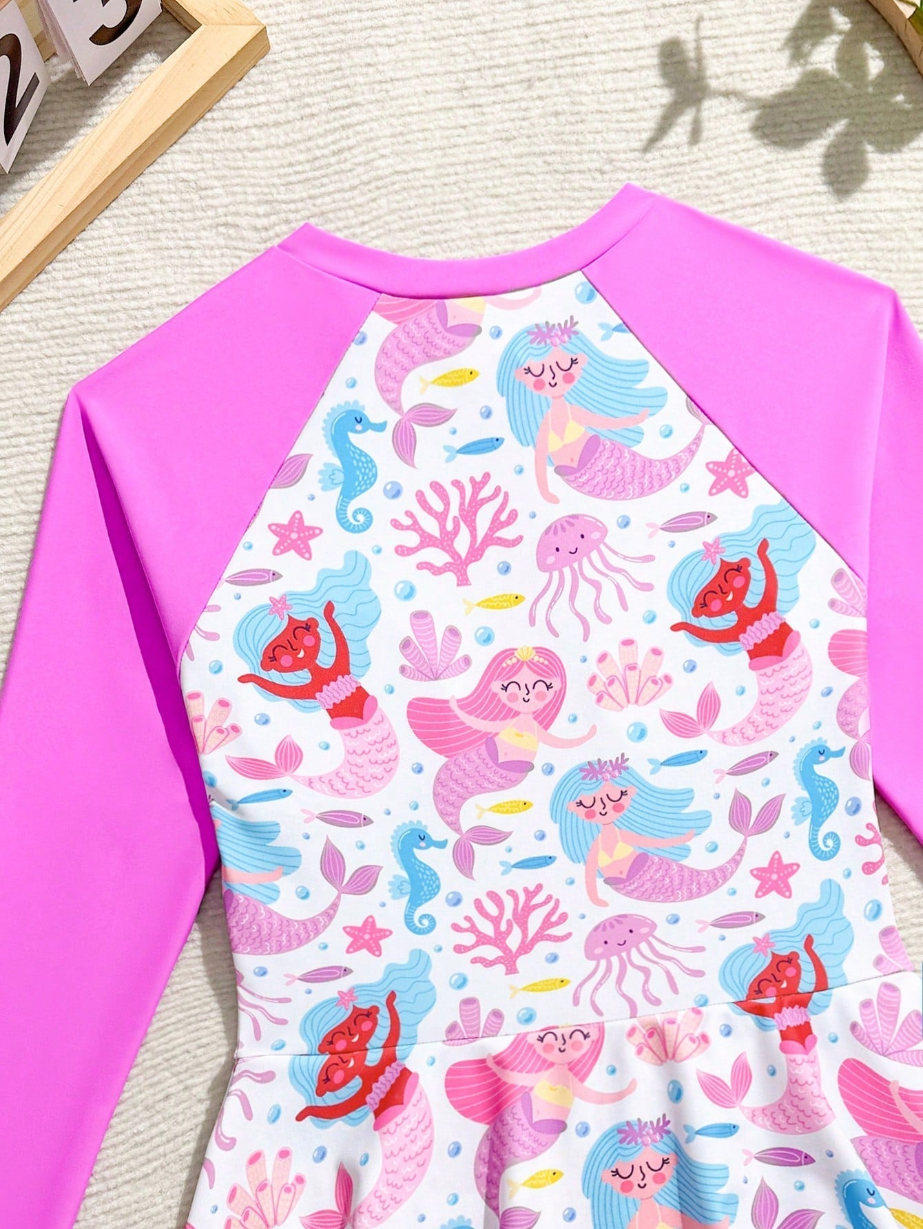 Tween girls one-piece rash guard swimsuit with long sleeves, high neck, front zipper, and ocean shell graphic print in a fitted style for beach, swimming, and vacation wear.